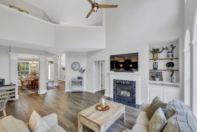 living room featuring ceiling fan with notable chandelier, decorative columns, dark hardwood / wood-style flooring, a high end fireplace, and high vaulted ceiling