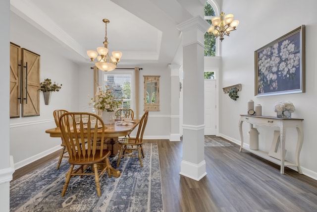 dining space with dark wood-type flooring, ornate columns, a notable chandelier, and a tray ceiling