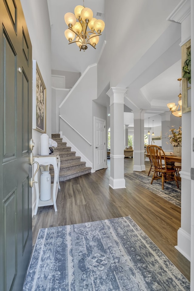 foyer featuring dark wood-type flooring, a notable chandelier, and decorative columns