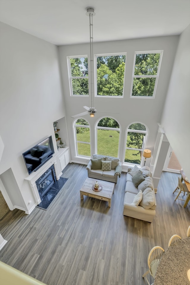 living room featuring a premium fireplace, ceiling fan, wood-type flooring, and a towering ceiling