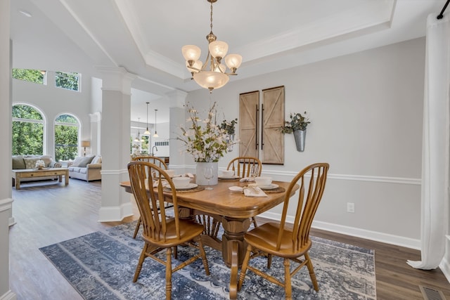 dining room featuring an inviting chandelier, a tray ceiling, dark wood-type flooring, and ornate columns