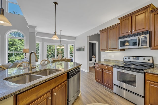 kitchen featuring appliances with stainless steel finishes, light stone countertops, sink, light hardwood / wood-style floors, and decorative light fixtures