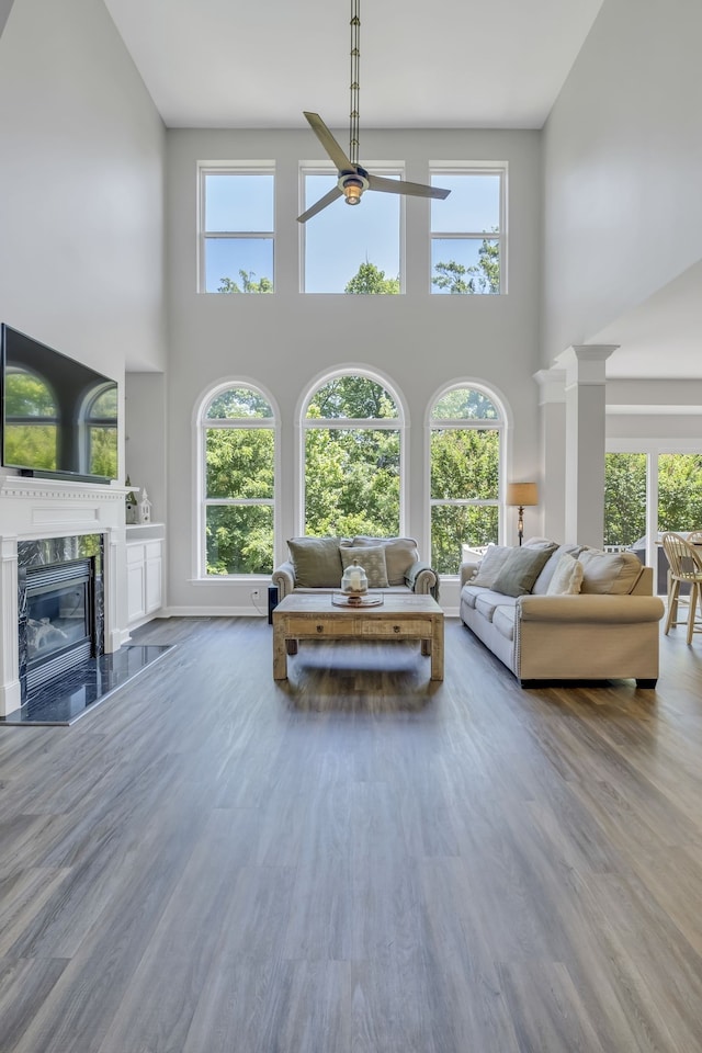 living room featuring a premium fireplace, hardwood / wood-style floors, a towering ceiling, and decorative columns