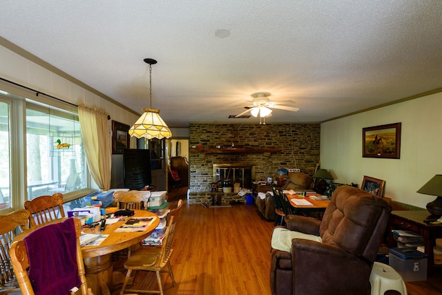 dining area featuring hardwood / wood-style floors, ceiling fan, a textured ceiling, a fireplace, and crown molding