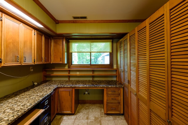 kitchen featuring built in desk, ornamental molding, and dark stone counters