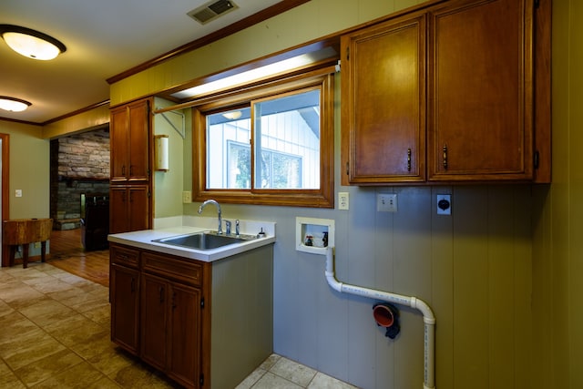 kitchen featuring a stone fireplace, ornamental molding, sink, and wooden walls