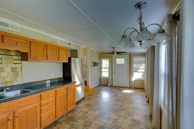 kitchen featuring ceiling fan, hanging light fixtures, sink, and stainless steel fridge