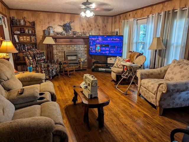 living room with ceiling fan, a textured ceiling, hardwood / wood-style flooring, a brick fireplace, and wood walls