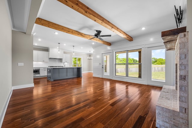 unfurnished living room featuring dark hardwood / wood-style floors, beamed ceiling, sink, and ceiling fan with notable chandelier