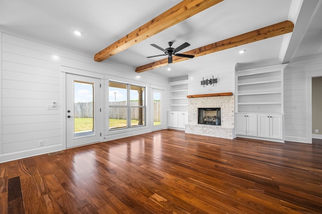 unfurnished living room with beam ceiling, ceiling fan, dark hardwood / wood-style flooring, a brick fireplace, and wood walls