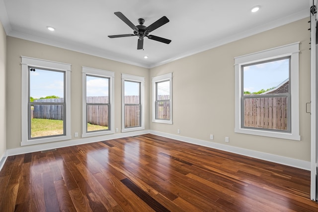 empty room featuring dark wood-type flooring, a barn door, crown molding, and ceiling fan