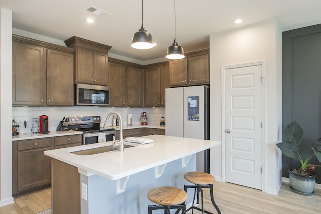 kitchen featuring decorative backsplash, a kitchen island with sink, stainless steel appliances, and hanging light fixtures