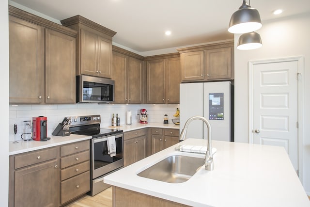 kitchen with hanging light fixtures, backsplash, sink, light hardwood / wood-style floors, and stainless steel appliances