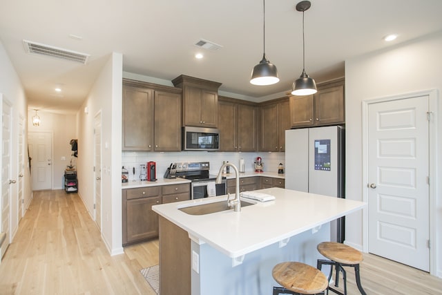 kitchen with tasteful backsplash, hanging light fixtures, a kitchen island with sink, sink, and stainless steel appliances