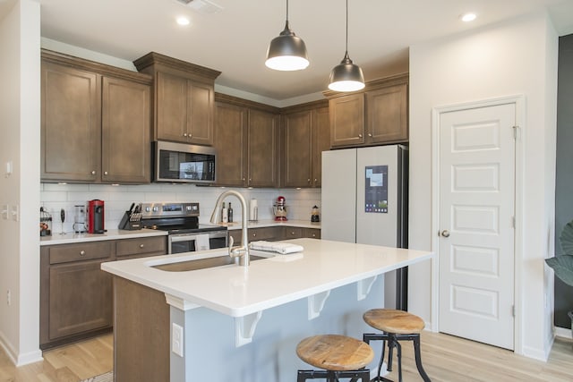 kitchen with stainless steel appliances, tasteful backsplash, decorative light fixtures, and a kitchen island with sink