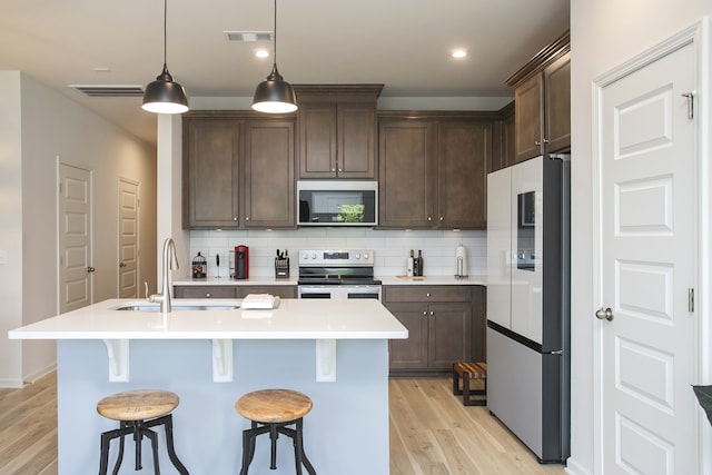 kitchen with sink, pendant lighting, appliances with stainless steel finishes, light hardwood / wood-style floors, and tasteful backsplash