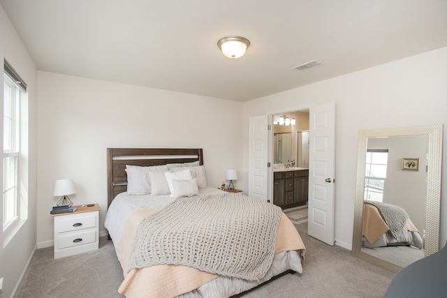 bedroom with ensuite bathroom and light colored carpet