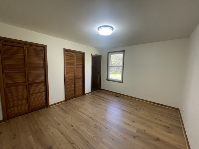 unfurnished bedroom with light hardwood / wood-style flooring and two closets