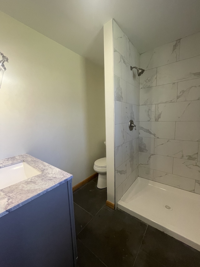 bathroom featuring toilet, vanity, tile patterned flooring, and a tile shower