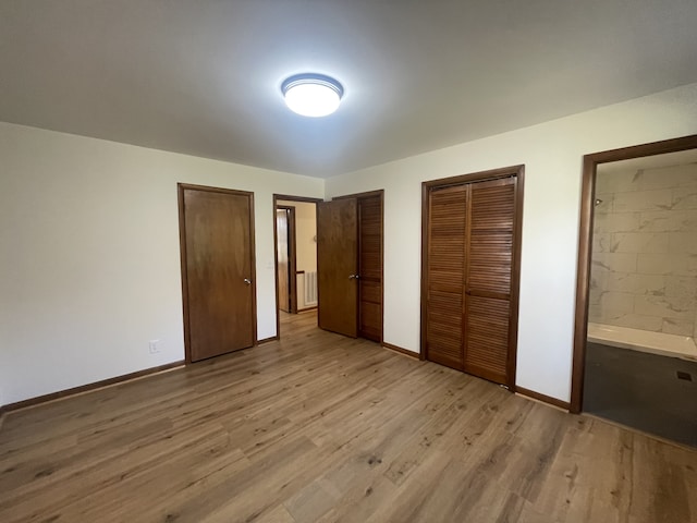 unfurnished bedroom with multiple closets, light hardwood / wood-style floors, and ensuite bath