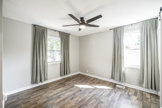 empty room featuring dark wood-type flooring, a barn door, and ceiling fan