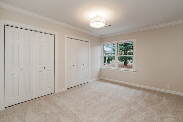 unfurnished bedroom featuring crown molding, light colored carpet, and two closets