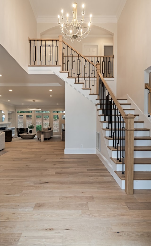 stairs featuring wood-type flooring, ornamental molding, a towering ceiling, and an inviting chandelier