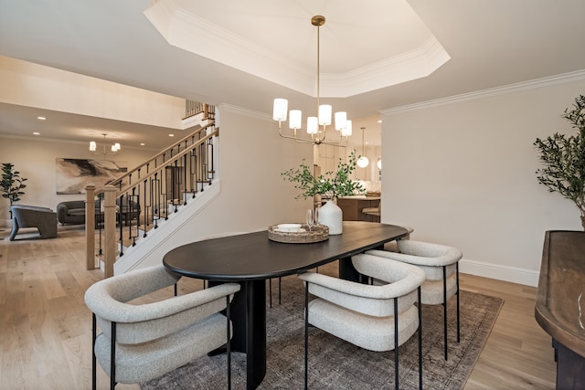 dining room with a notable chandelier, light wood-type flooring, crown molding, and a tray ceiling