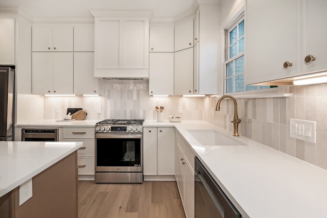 kitchen with appliances with stainless steel finishes, light wood-type flooring, tasteful backsplash, sink, and white cabinets