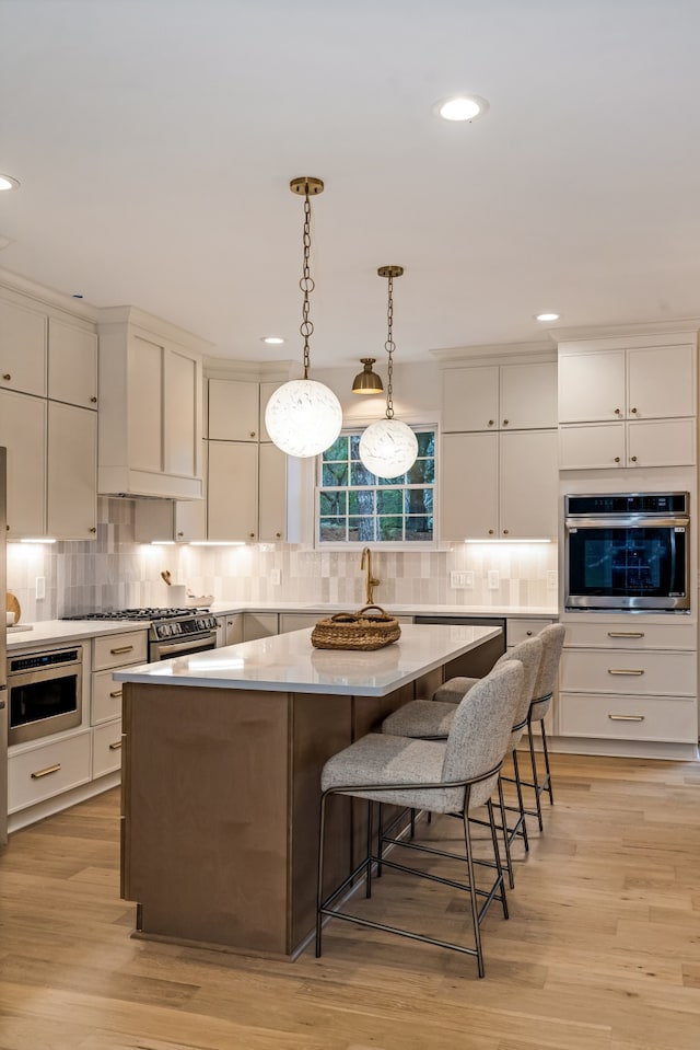 kitchen featuring stainless steel oven, a center island, hanging light fixtures, light hardwood / wood-style floors, and a breakfast bar