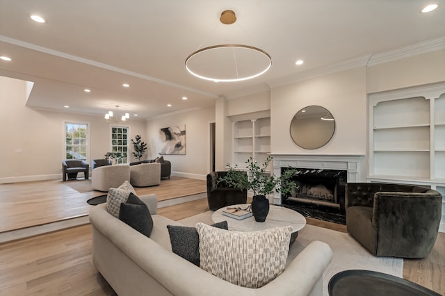 living room with light hardwood / wood-style flooring, a high end fireplace, a notable chandelier, and ornamental molding