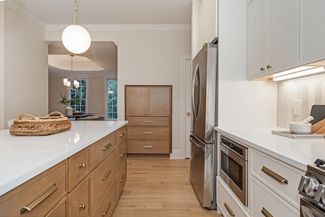 kitchen featuring ornamental molding, stainless steel appliances, pendant lighting, white cabinets, and light hardwood / wood-style floors