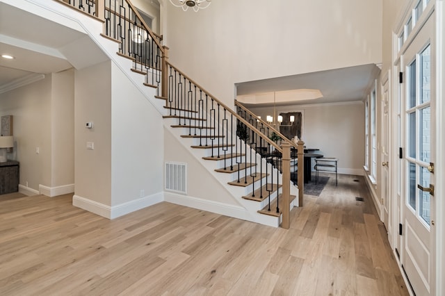 entrance foyer featuring a high ceiling, light wood-type flooring, an inviting chandelier, and ornamental molding