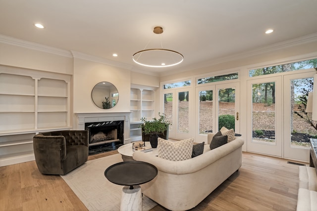 living room with french doors, crown molding, built in shelves, a premium fireplace, and light hardwood / wood-style floors