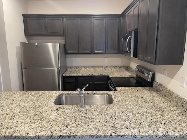 kitchen with light stone countertops, sink, stainless steel appliances, and dark brown cabinets