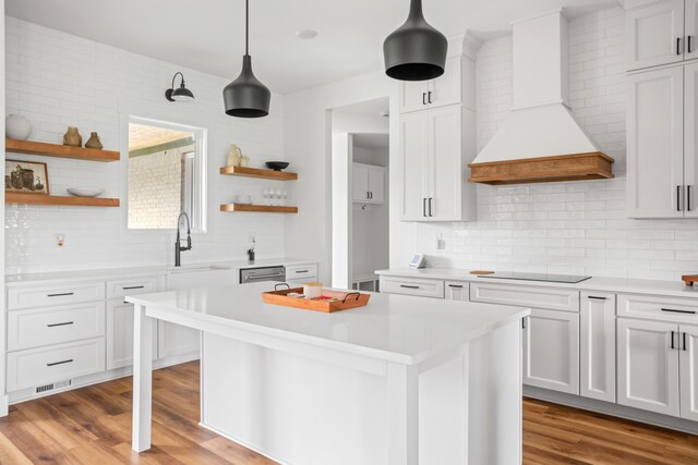 kitchen with hanging light fixtures, custom exhaust hood, white cabinets, and light hardwood / wood-style flooring