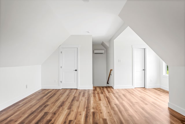 additional living space featuring lofted ceiling, a wall mounted AC, and light wood-type flooring