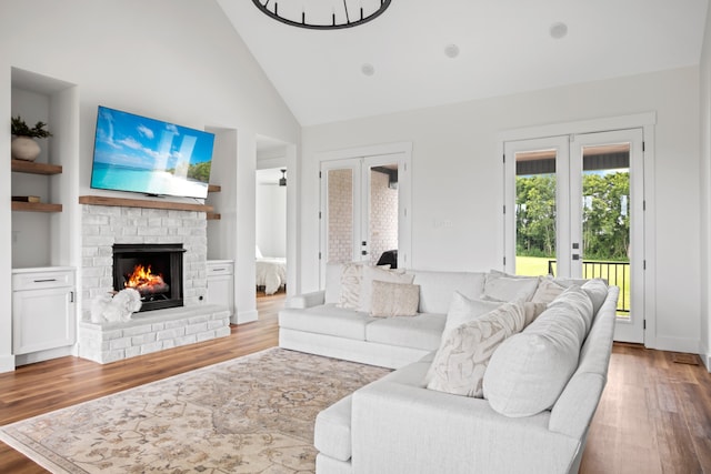 living room with french doors, light hardwood / wood-style floors, high vaulted ceiling, and a fireplace