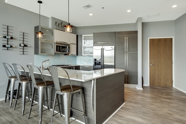 kitchen featuring light hardwood / wood-style floors, stainless steel appliances, hanging light fixtures, and a kitchen breakfast bar