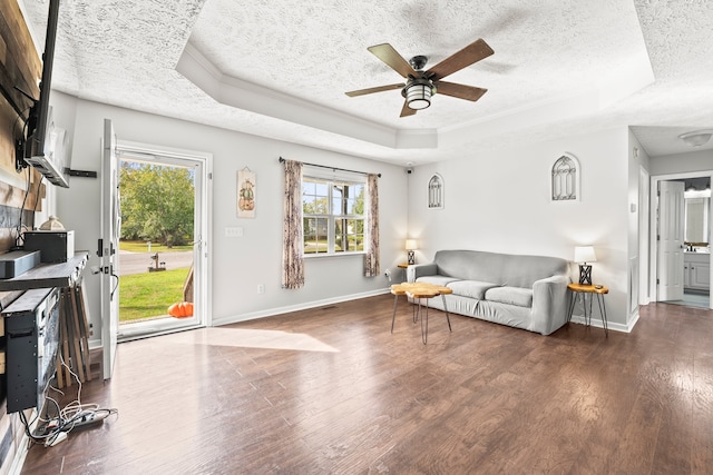 living room with ceiling fan, a textured ceiling, dark hardwood / wood-style flooring, and a tray ceiling