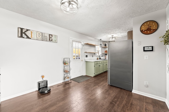 kitchen with dark hardwood / wood-style floors, a textured ceiling, backsplash, green cabinetry, and stainless steel fridge