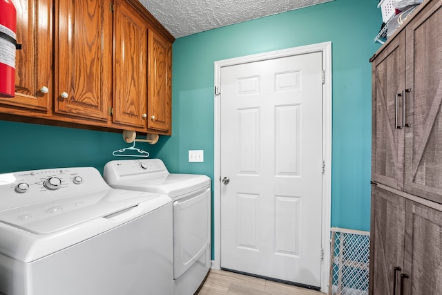 washroom with cabinets, washing machine and clothes dryer, light hardwood / wood-style floors, and a textured ceiling