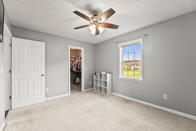 unfurnished bedroom featuring a spacious closet, light carpet, ceiling fan, and a closet