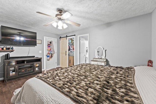 bedroom with ceiling fan, a barn door, dark hardwood / wood-style floors, and a textured ceiling