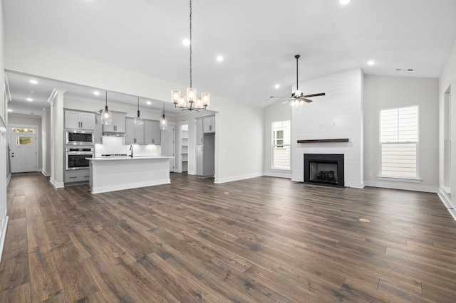 unfurnished living room featuring a large fireplace, a healthy amount of sunlight, ceiling fan, and dark hardwood / wood-style flooring