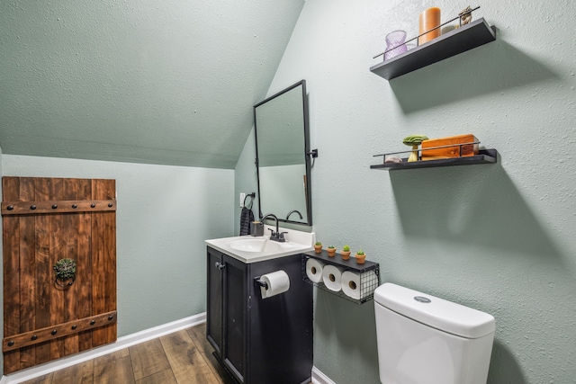 bathroom with lofted ceiling, toilet, wood finished floors, vanity, and baseboards