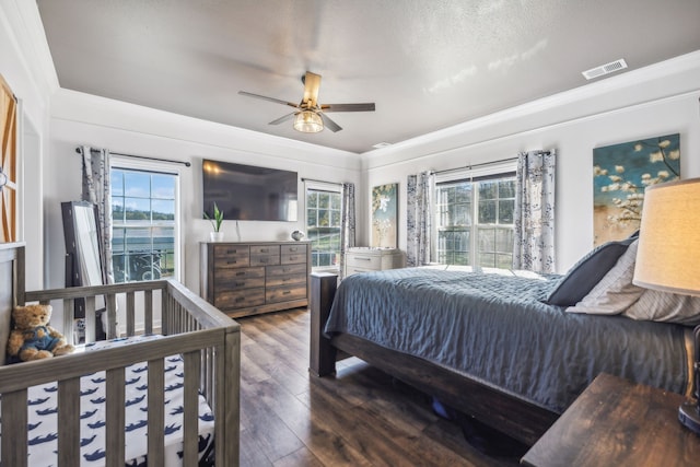 bedroom with dark wood-style floors, ceiling fan, visible vents, and crown molding