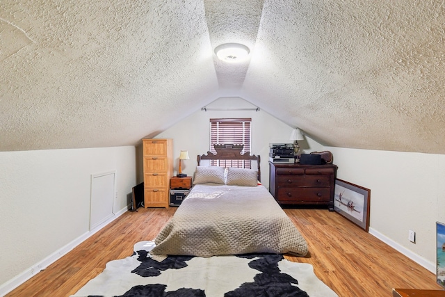 bedroom featuring light hardwood / wood-style floors, a textured ceiling, and lofted ceiling