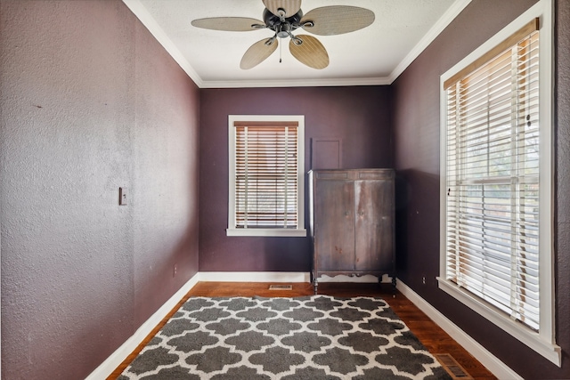 unfurnished bedroom featuring multiple windows, dark wood-type flooring, crown molding, and ceiling fan