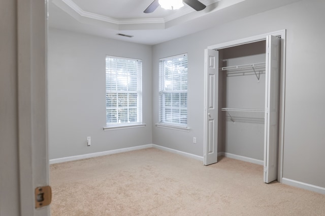 unfurnished bedroom featuring light carpet, a raised ceiling, ceiling fan, a closet, and crown molding